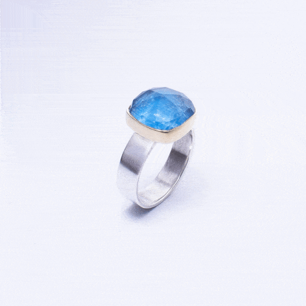 Handmade sterling silver and 18k gold ring with doublet made of natural crystal quartz and apatite gemstones, in a square shape. The band of the ring is made of sterling silver and the outline of the bezel is made of 18 carats gold. The doublet consists of two layers of stones. The upper stone is faceted crystal quartz and the stone at the bottom is apatite. Buy online shop.